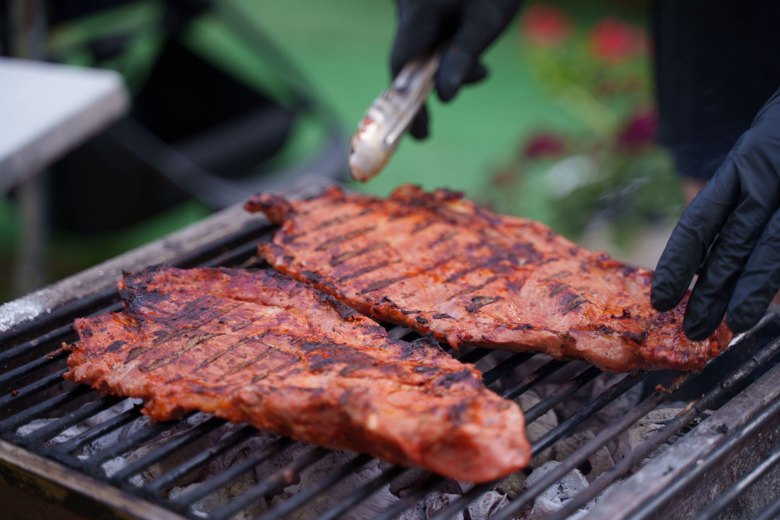 Close-up of juicy grilled meat cooking on an outdoor BBQ with tongs handling ribs.